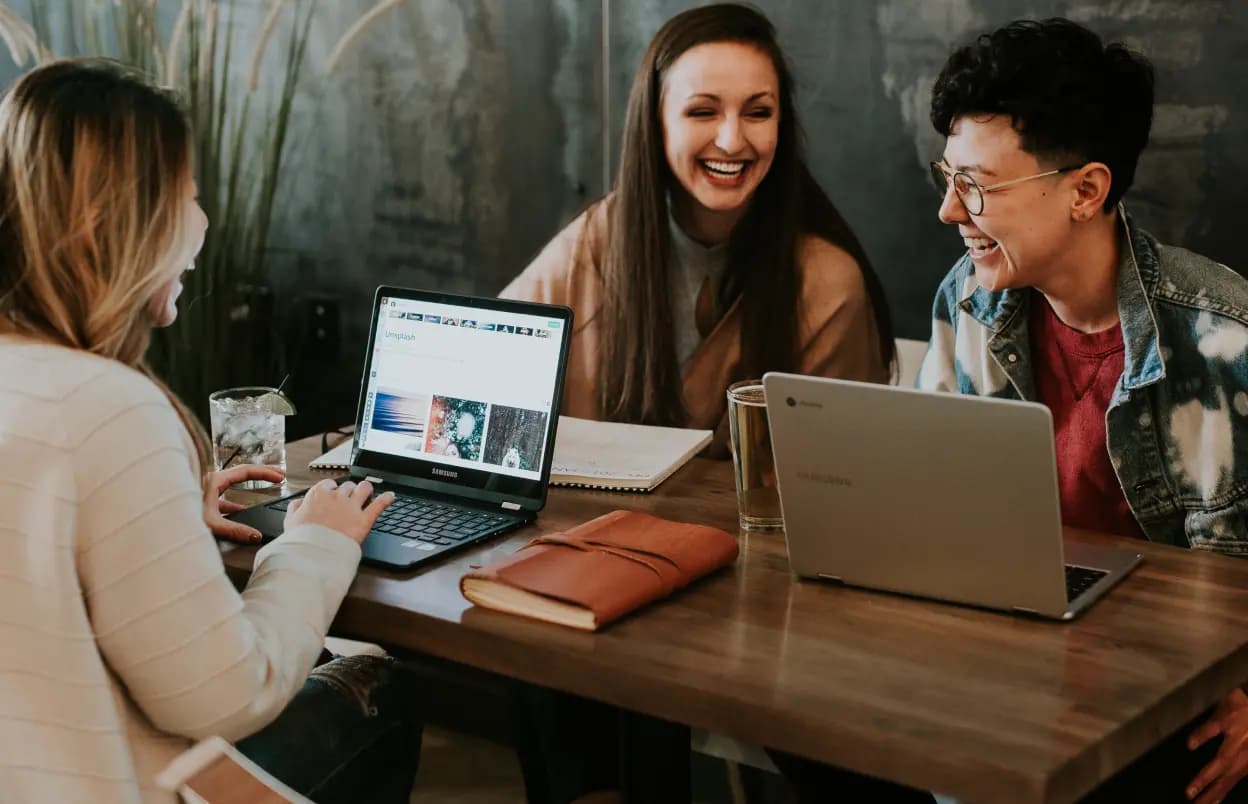 Group working session shot, with three individuals working with laptops and exchanging a humorous quip